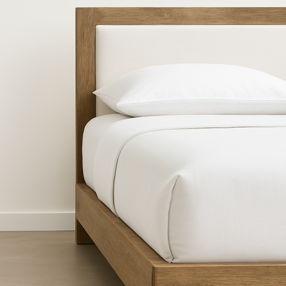 Wooden bed with white bedding against a plain wall
